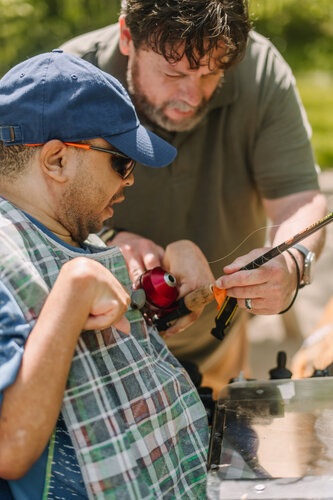 Man helping another man with his fishing rod